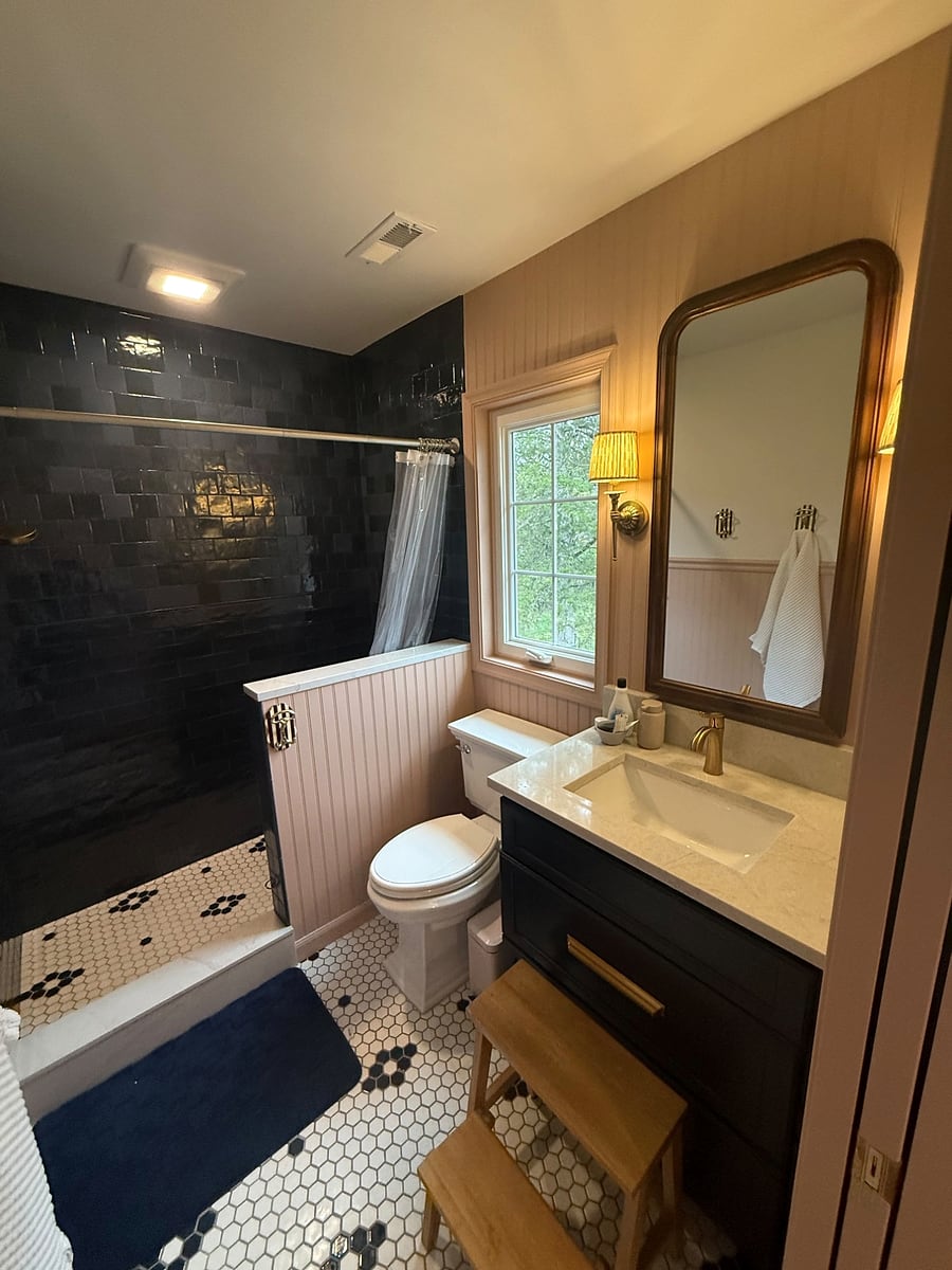 Bathroom remodel with a navy vanity, brass fixtures and a dark tile shower