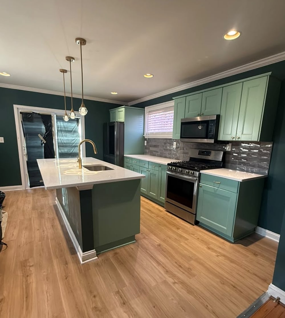 Sage-green kitchen with a long island and brass pendants