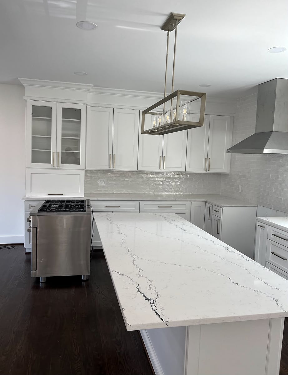 White kitchen with a large veined stone island and a linear pendant